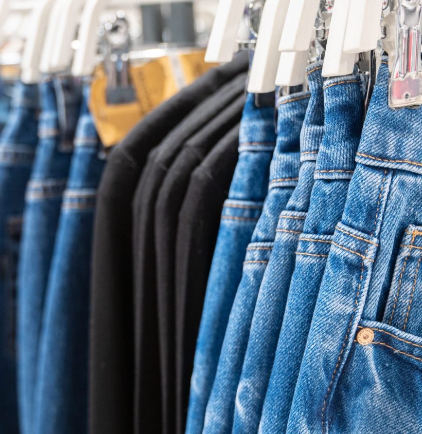 Denim jeans store detail. Row of blue jeans hung on plastic hangers in store. Many jeans are hanging on counter. High quality photo